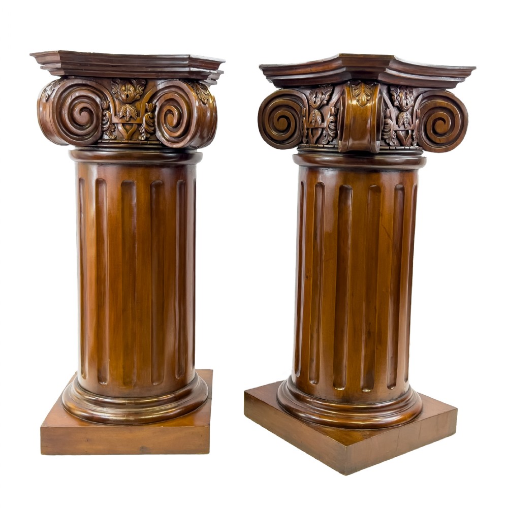 A pair of carved warm brown wooden pedestals styled as classical Ionic columns with fluted shafts and square bases.