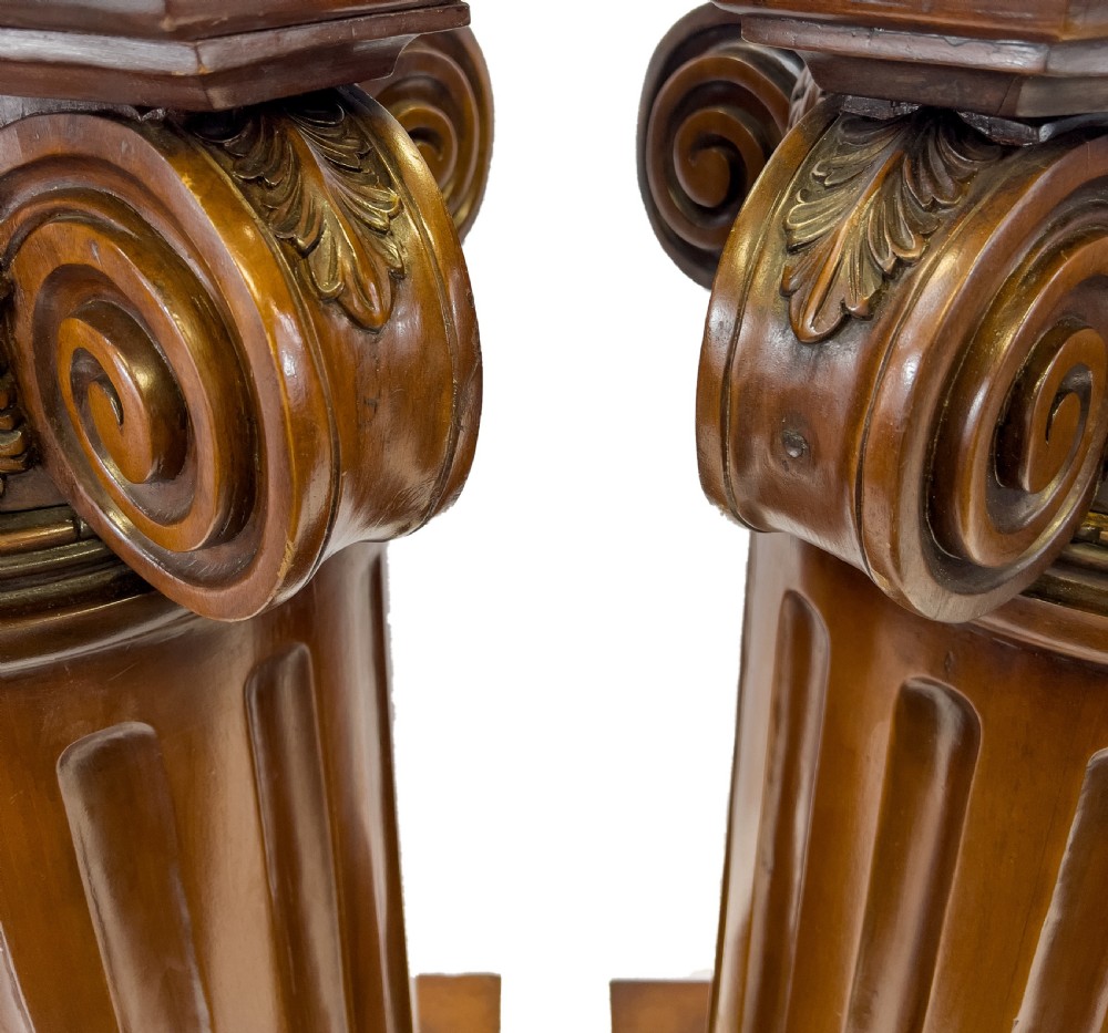 A pair of carved warm brown wooden pedestals styled as classical Ionic columns with fluted shafts and square bases. View II