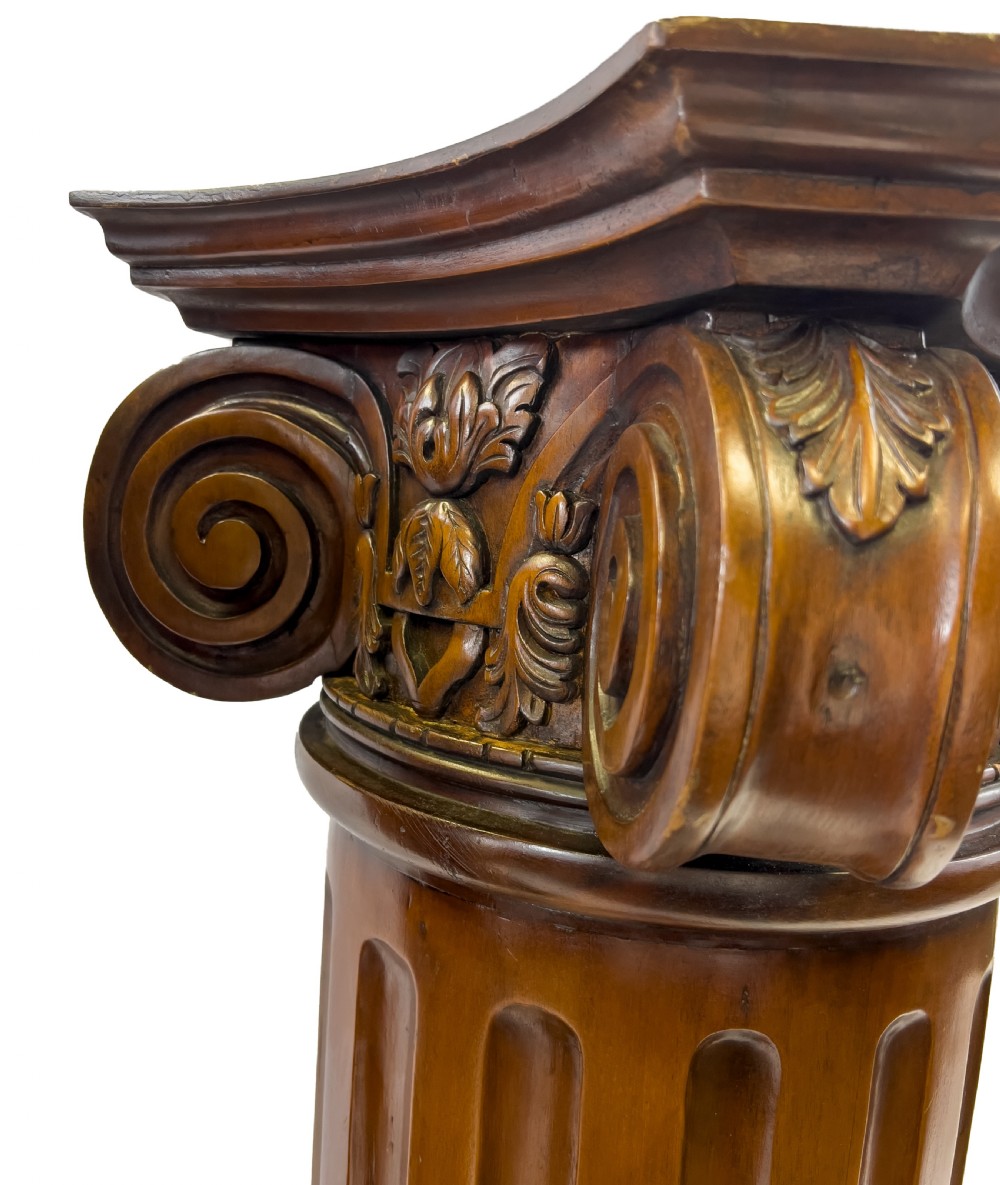 A pair of carved warm brown wooden pedestals styled as classical Ionic columns with fluted shafts and square bases. View III