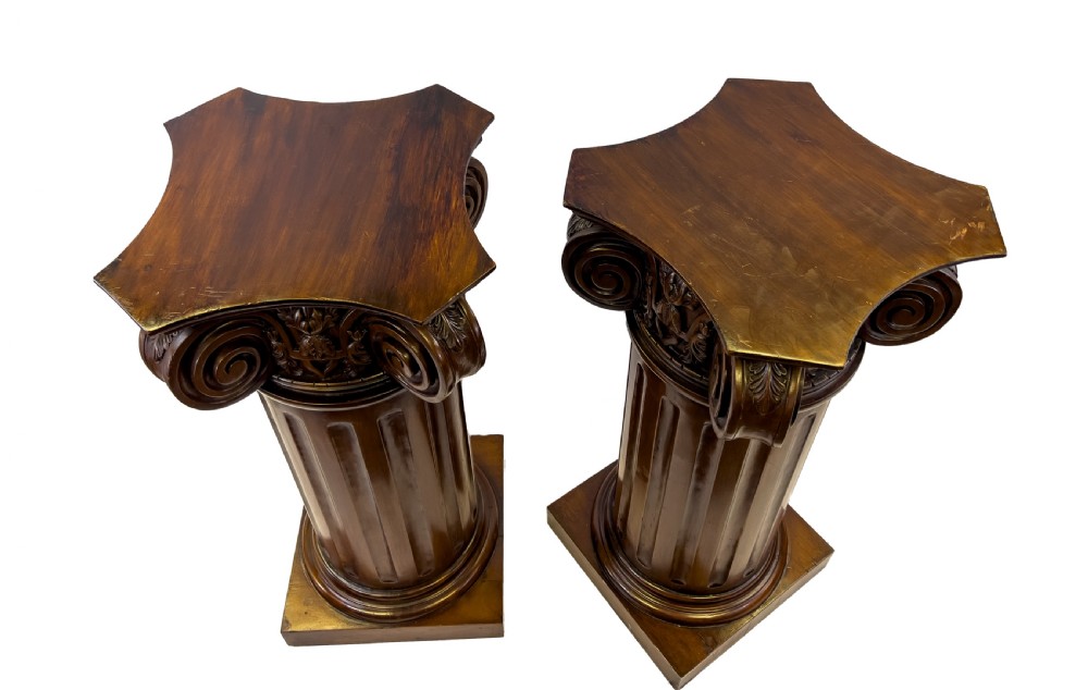 A pair of carved warm brown wooden pedestals styled as classical Ionic columns with fluted shafts and square bases. View VI