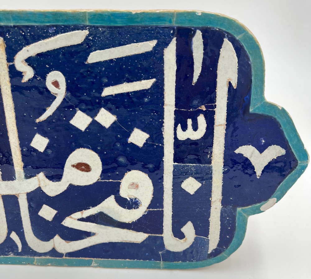 An elongated cobalt blue ceramic tile featuring white Arabic calligraphic script framed within a turquoise border. View III