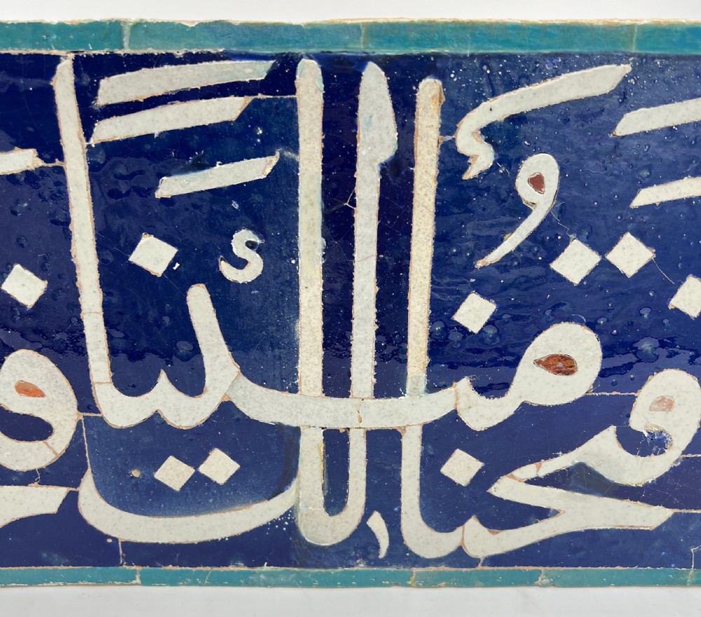 An elongated cobalt blue ceramic tile featuring white Arabic calligraphic script framed within a turquoise border. View IV