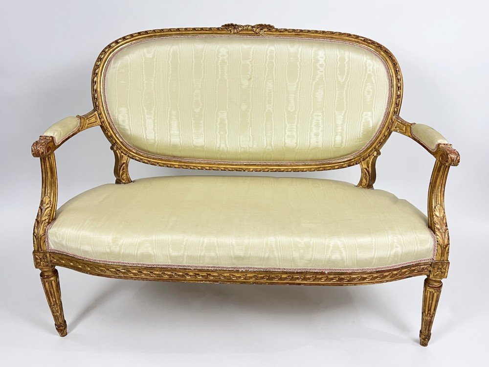 A five-piece 19th-century French Louis XVI style giltwood salon suite featuring a three-seater settee and four matching fauteuil armchairs upholstered in cream fabric. View II