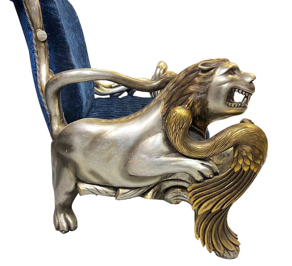An ornate two-seater sofa featuring deep blue crushed velvet upholstery and a gilded wooden frame carved with a lion on one armrest and branch motifs on the other. View V