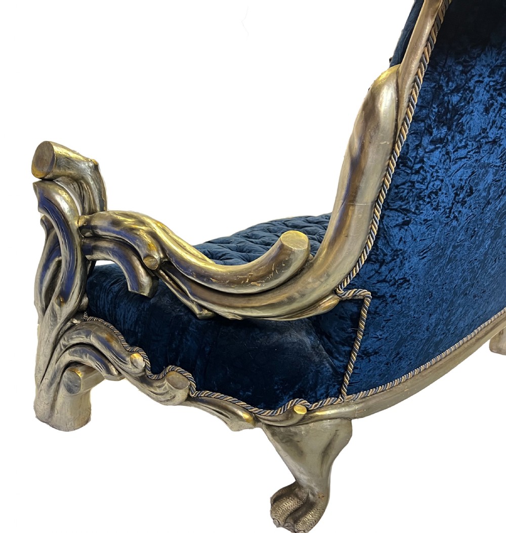 An ornate two-seater sofa featuring deep blue crushed velvet upholstery and a gilded wooden frame carved with a lion on one armrest and branch motifs on the other. View VIII