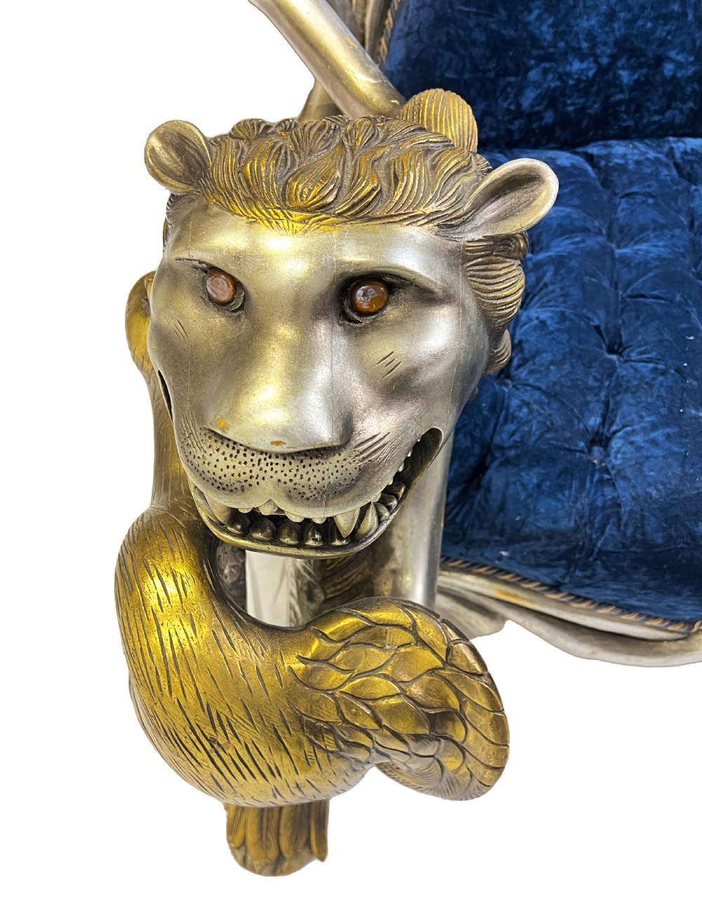 An ornate two-seater sofa featuring deep blue crushed velvet upholstery and a gilded wooden frame carved with a lion on one armrest and branch motifs on the other. View X