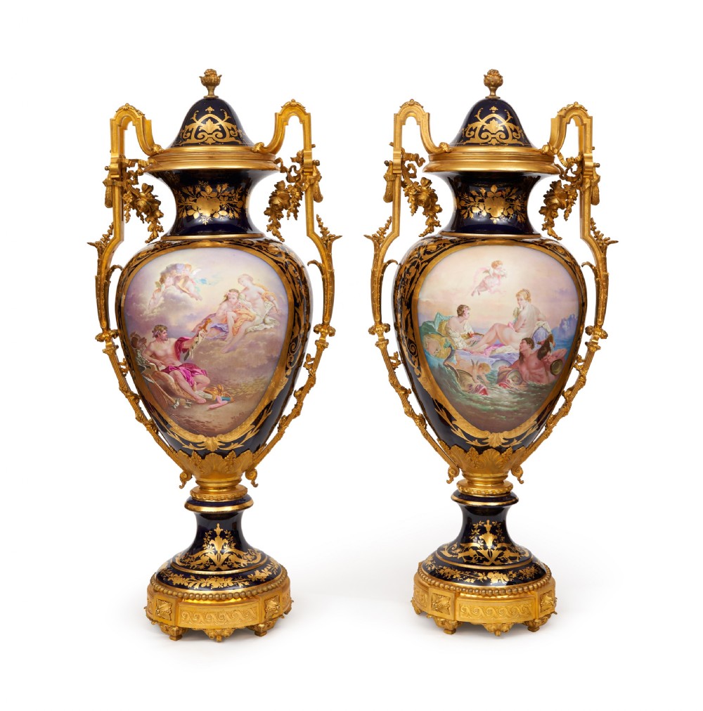 A pair of large French Sevres style cobalt blue porcelain lidded urns featuring hand-painted mythological scenes and elaborate gilded ormolu handles.