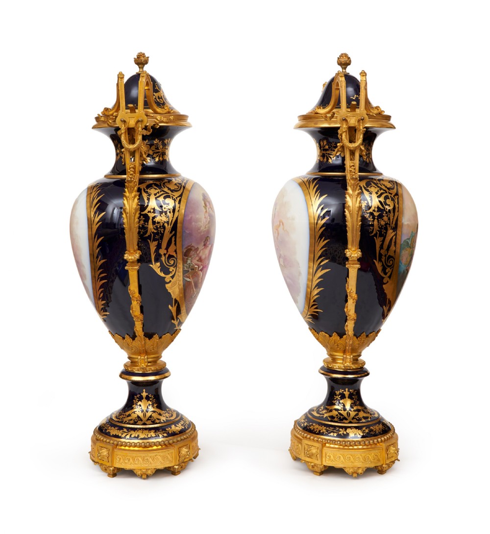 A pair of large French Sevres style cobalt blue porcelain lidded urns featuring hand-painted mythological scenes and elaborate gilded ormolu handles. View II