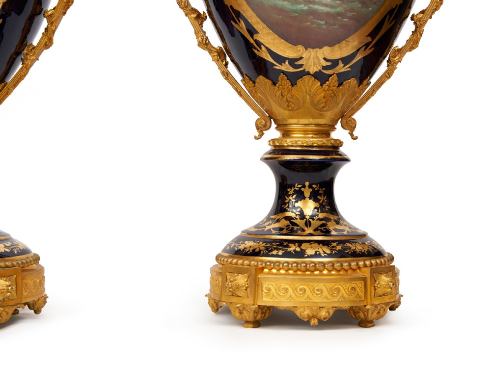 A pair of large French Sevres style cobalt blue porcelain lidded urns featuring hand-painted mythological scenes and elaborate gilded ormolu handles. View VIII