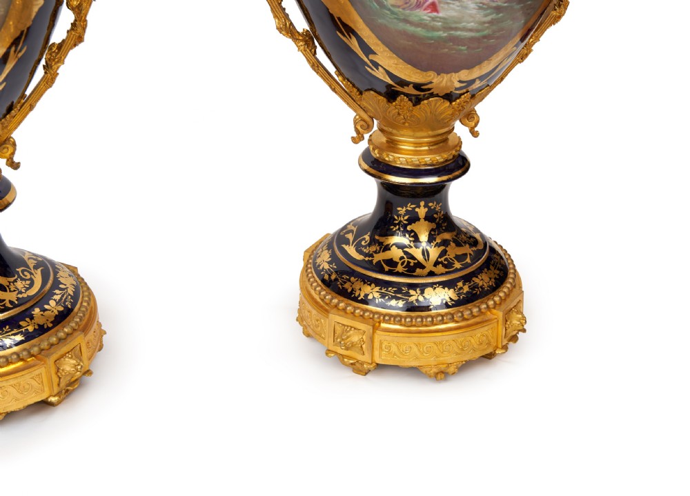 A pair of large French Sevres style cobalt blue porcelain lidded urns featuring hand-painted mythological scenes and elaborate gilded ormolu handles. View IX