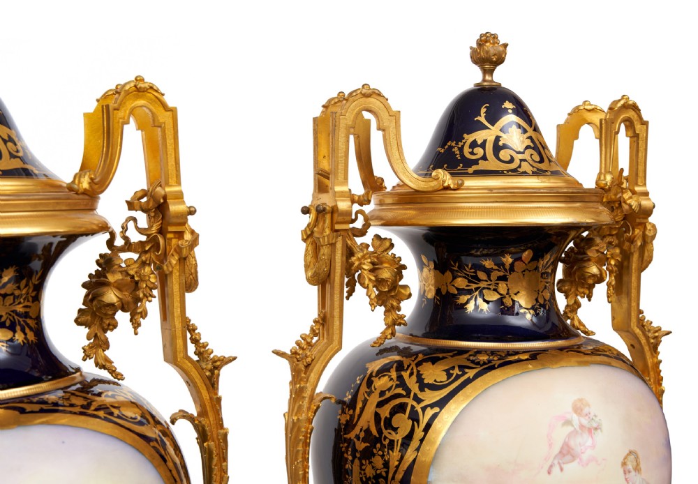 A pair of large French Sevres style cobalt blue porcelain lidded urns featuring hand-painted mythological scenes and elaborate gilded ormolu handles. View X