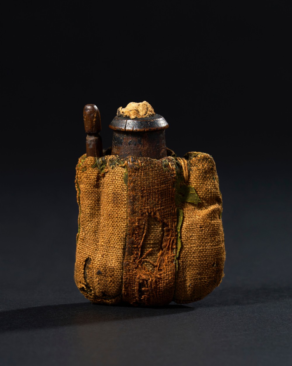 An ancient Egyptian wooden kohl vessel with an applicator rod, bound in textured ochre linen cloth.