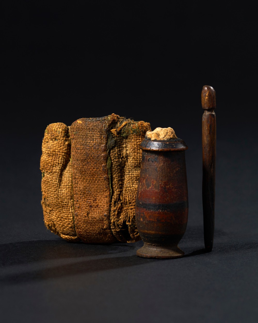 An ancient Egyptian wooden kohl vessel with an applicator rod, bound in textured ochre linen cloth. View II