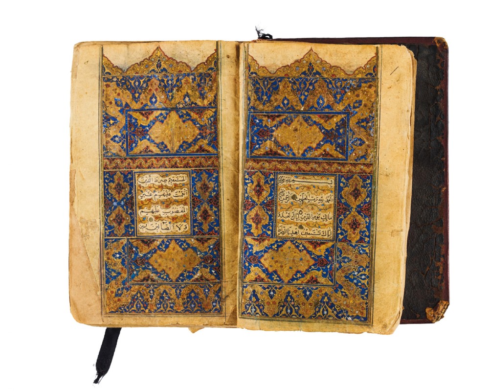 An open fifteenth-century Persian Timurid Quran manuscript featuring gold leaf and lapis lazuli blue arabesque illuminated frontispiece panels with Arabic calligraphy.