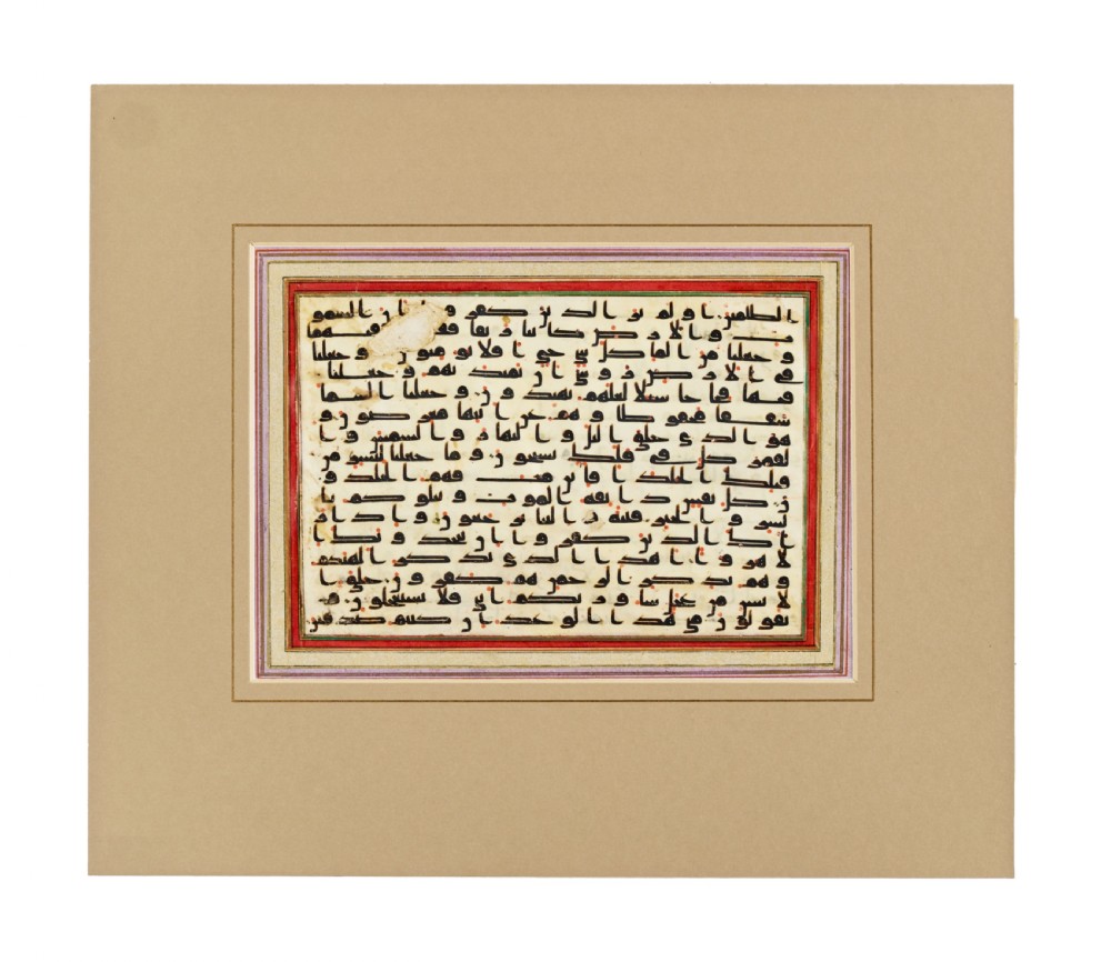 A rectangular vellum page featuring horizontal lines of dark Kufic Arabic script with small red dots, presented within a framed mount.