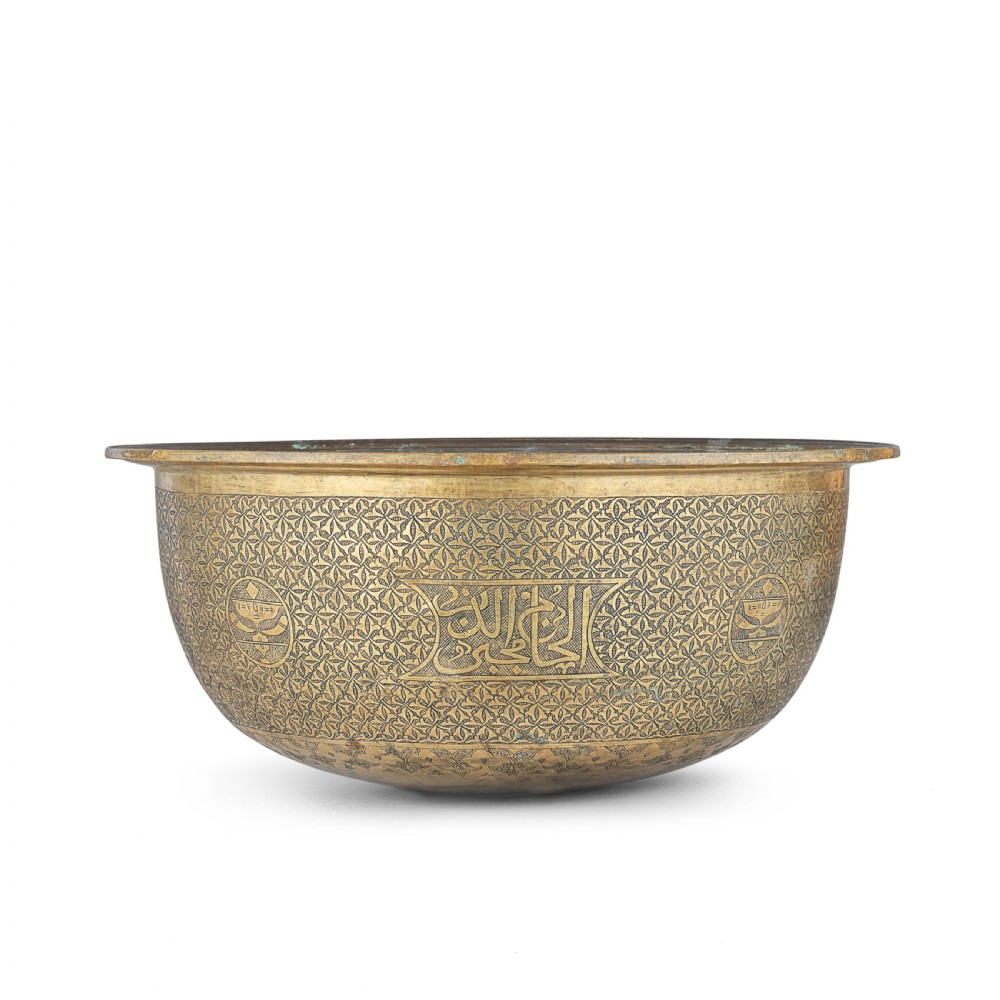 A large round brass basin featuring continuous hand-engraved Arabic calligraphic script and all-over arabesque motifs along its exterior walls. View II