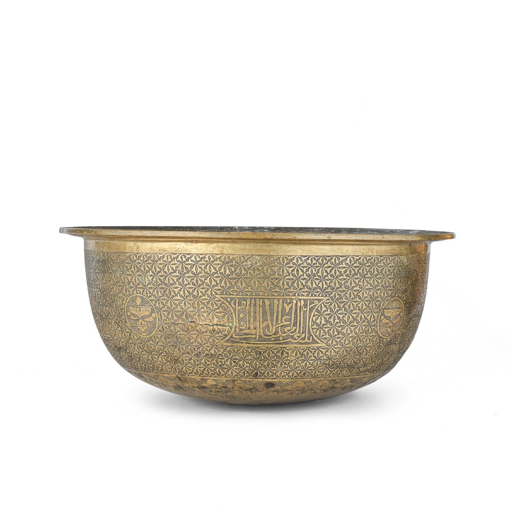 A large round brass basin featuring continuous hand-engraved Arabic calligraphic script and all-over arabesque motifs along its exterior walls. View IV