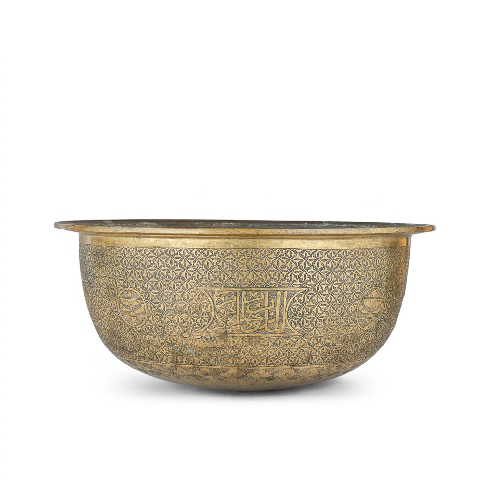 A large round brass basin featuring continuous hand-engraved Arabic calligraphic script and all-over arabesque motifs along its exterior walls. View V
