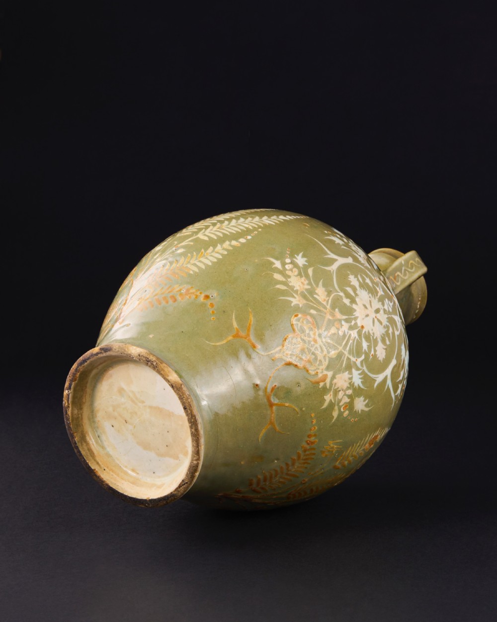 A large 17th-century Safavid pottery vase with twin handles, finished in an olive-green celadon glaze and painted with white and brown botanical foliage motifs. View V