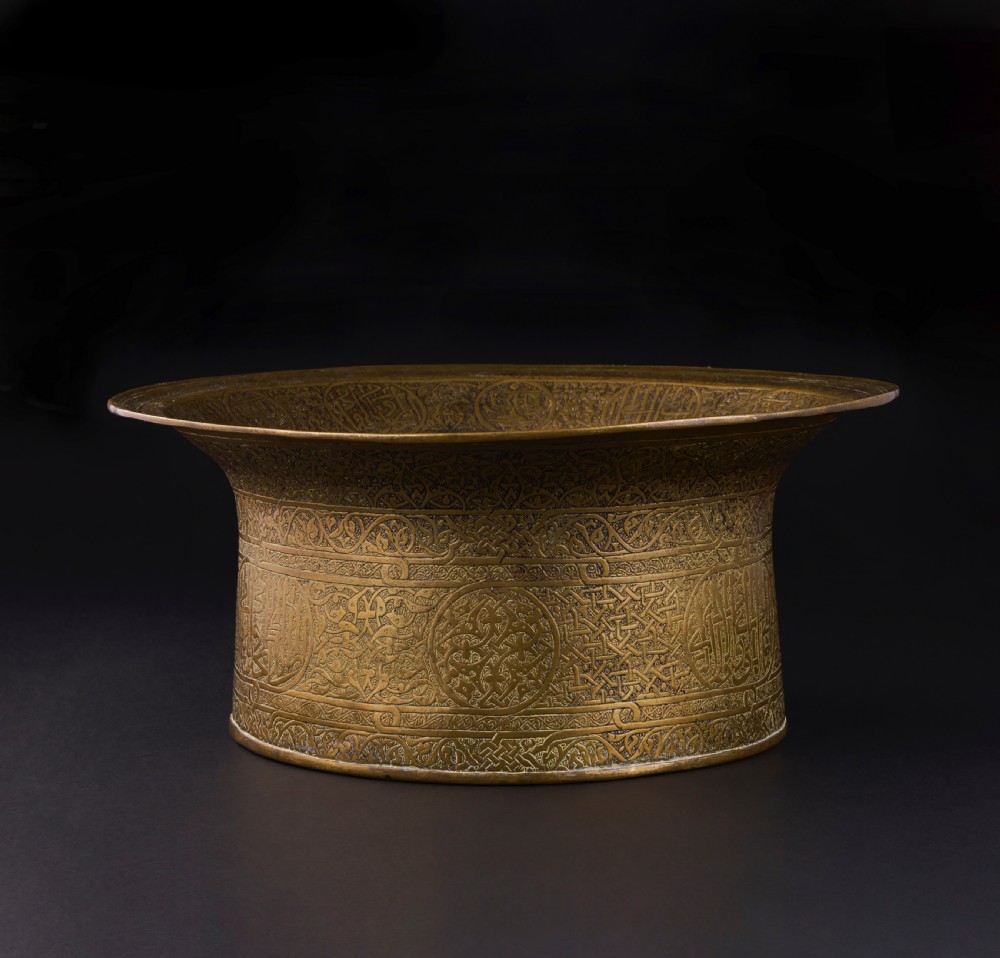 A 16th-century Mamluk brass basin featuring a wide flared rim, intricate hand-engraved Arabic calligraphy, arabesques, and geometric patterns. View II