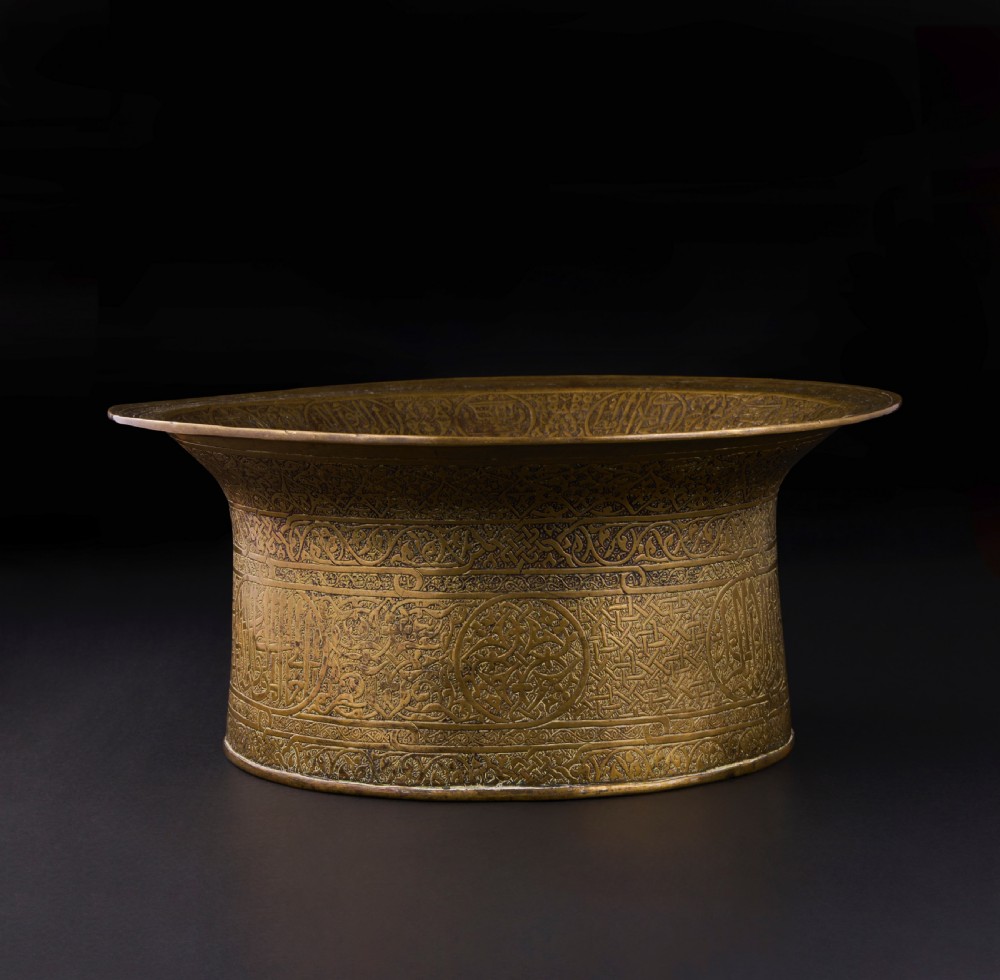A 16th-century Mamluk brass basin featuring a wide flared rim, intricate hand-engraved Arabic calligraphy, arabesques, and geometric patterns. View IV