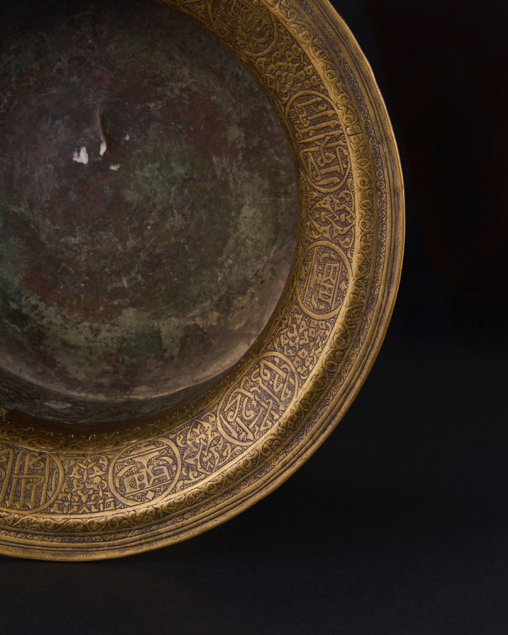 A 16th-century Mamluk brass basin featuring a wide flared rim, intricate hand-engraved Arabic calligraphy, arabesques, and geometric patterns. View VI