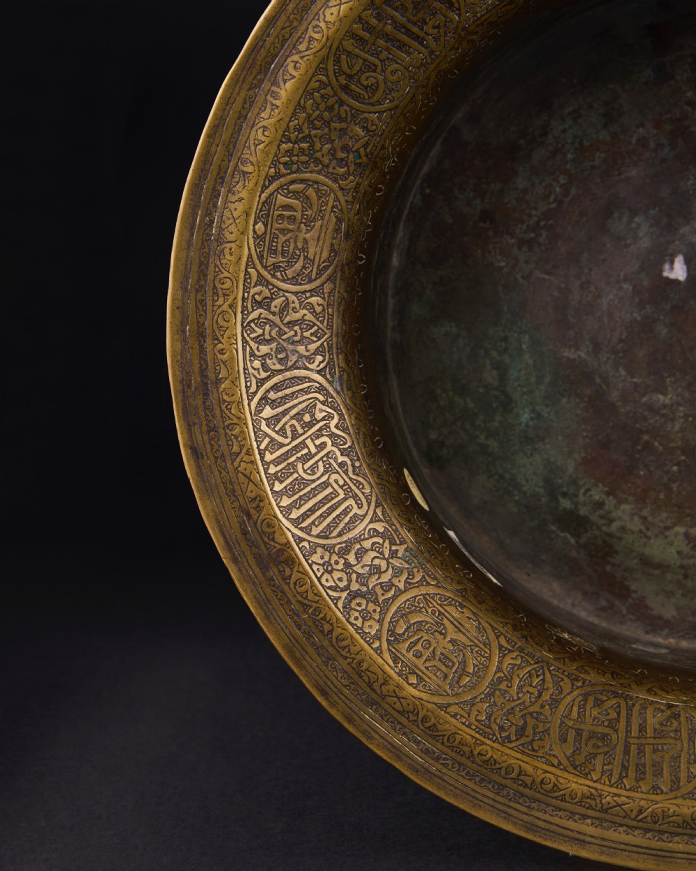 A 16th-century Mamluk brass basin featuring a wide flared rim, intricate hand-engraved Arabic calligraphy, arabesques, and geometric patterns. View VII