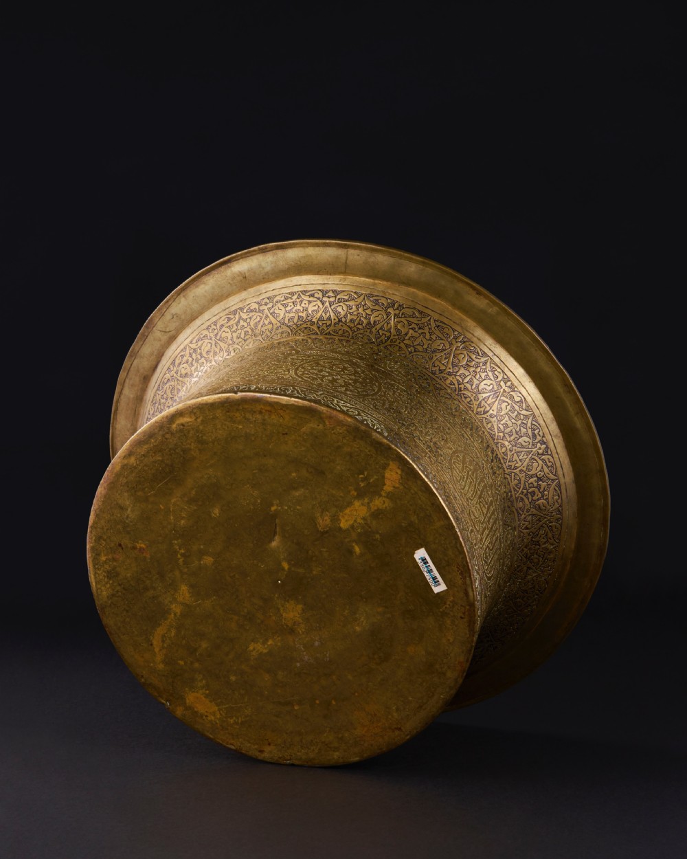 A 16th-century Mamluk brass basin featuring a wide flared rim, intricate hand-engraved Arabic calligraphy, arabesques, and geometric patterns. View VIII