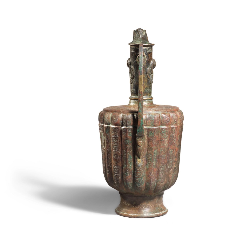 A 12th-century Persian bronze ewer featuring a fluted body, high handle with lion motif, raised spout, and copper and silver inlaid calligraphic bands. View IV