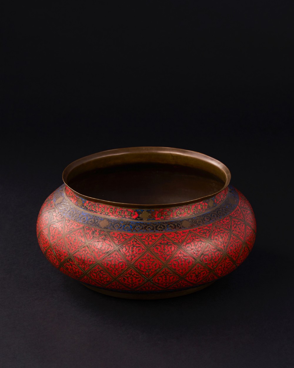 A bulbous Safavid period brass bowl featuring red and blue enamelled geometric lattice patterns around its body. View II