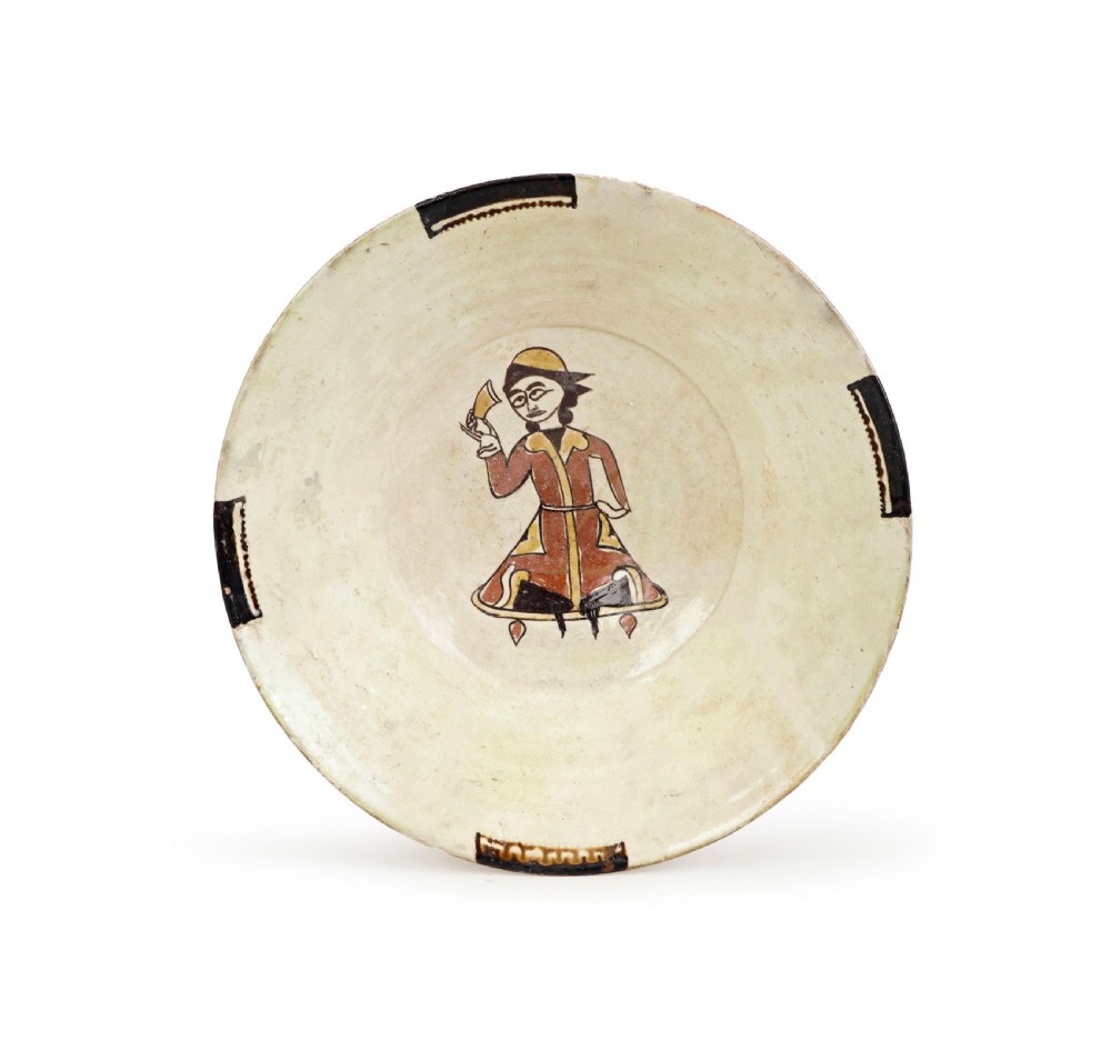 A tenth-century Nishapur slip-painted earthenware bowl featuring a central seated figure holding a vessel against a cream background.