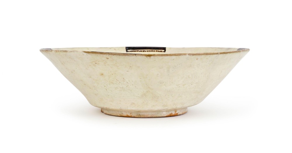 A tenth-century Nishapur slip-painted earthenware bowl featuring a central seated figure holding a vessel against a cream background. View II