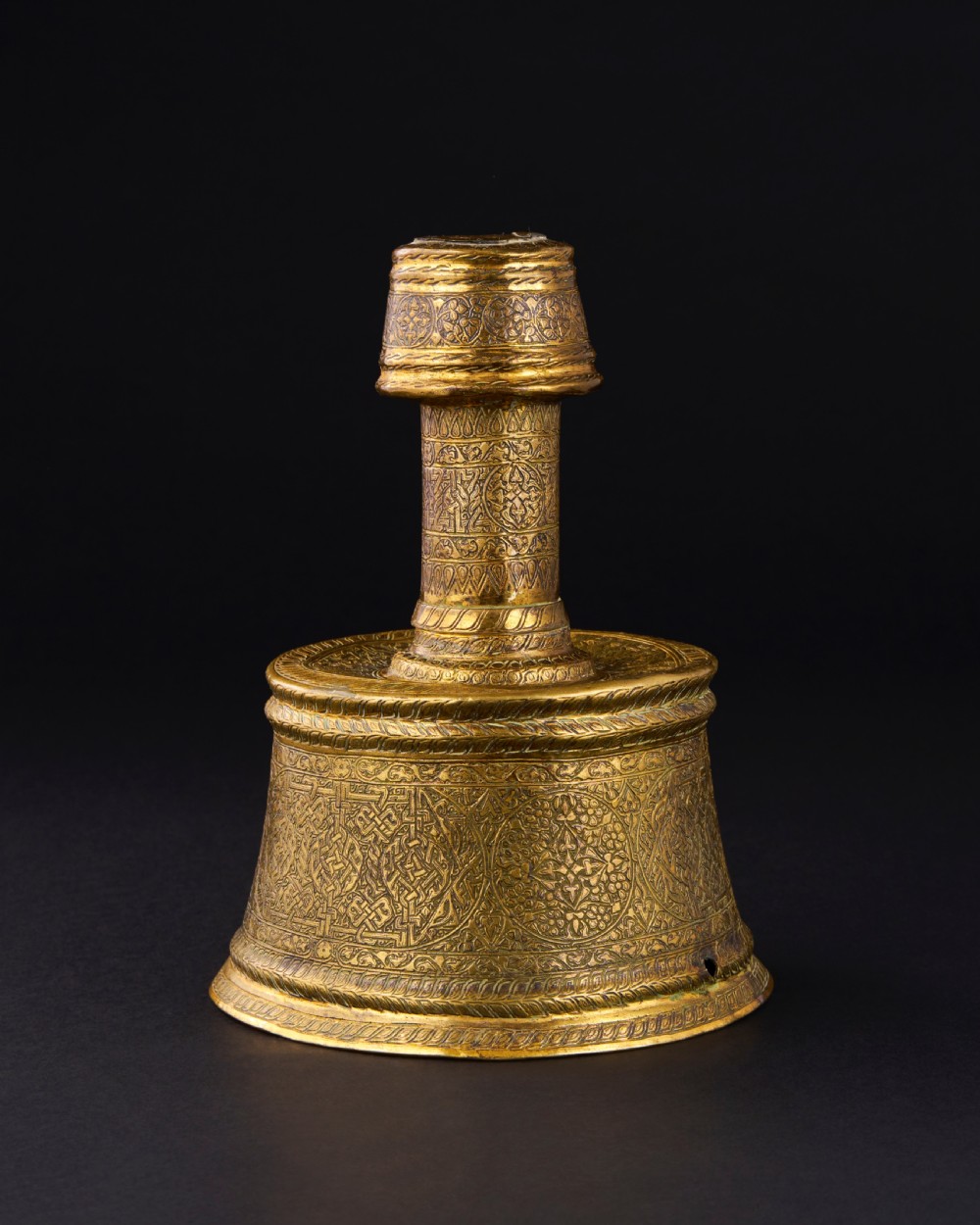 A 15th-century Mamluk brass candlestick featuring a wide flared base and cylindrical stem decorated with intricate geometric and arabesque engravings. View II