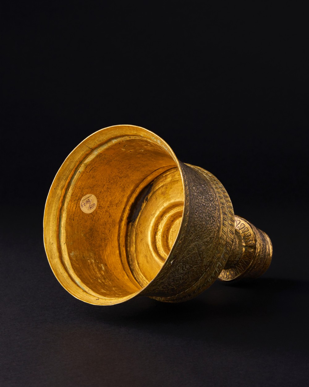 A 15th-century Mamluk brass candlestick featuring a wide flared base and cylindrical stem decorated with intricate geometric and arabesque engravings. View III