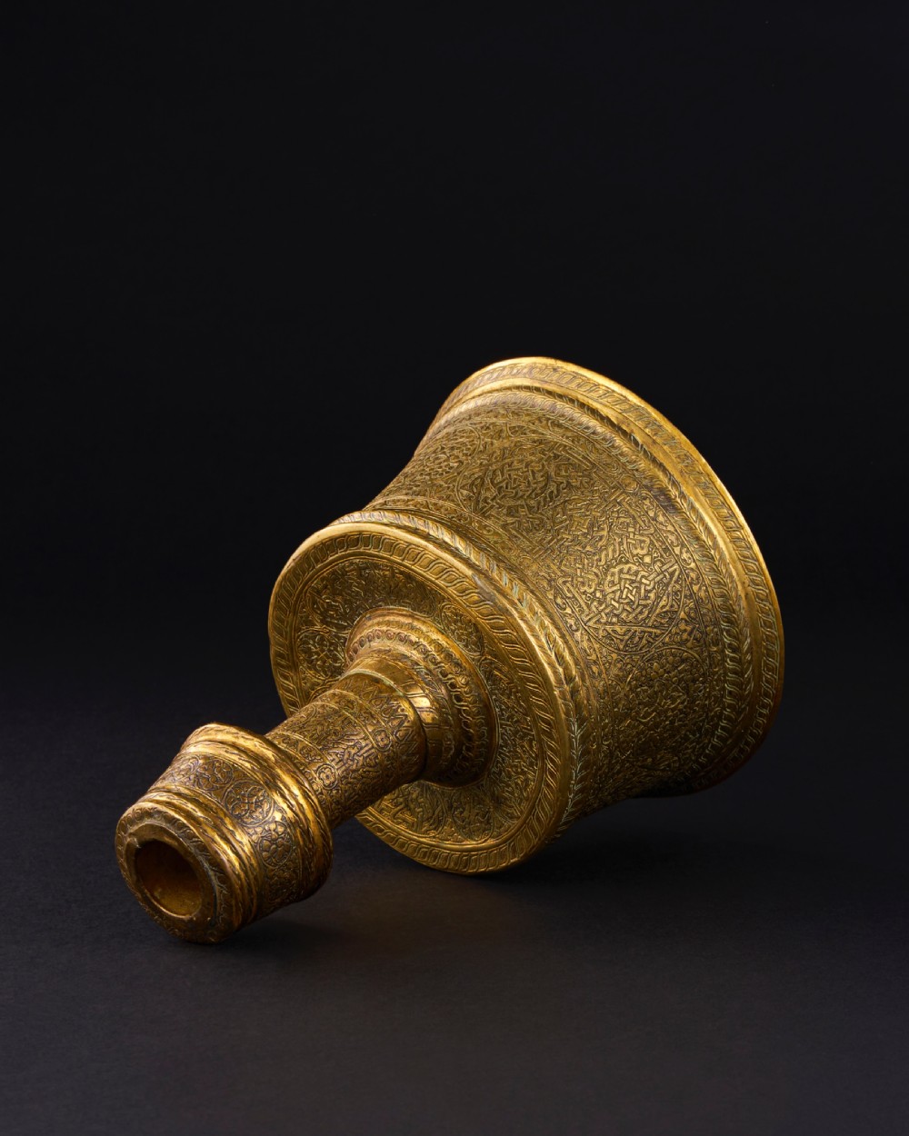 A 15th-century Mamluk brass candlestick featuring a wide flared base and cylindrical stem decorated with intricate geometric and arabesque engravings. View IV
