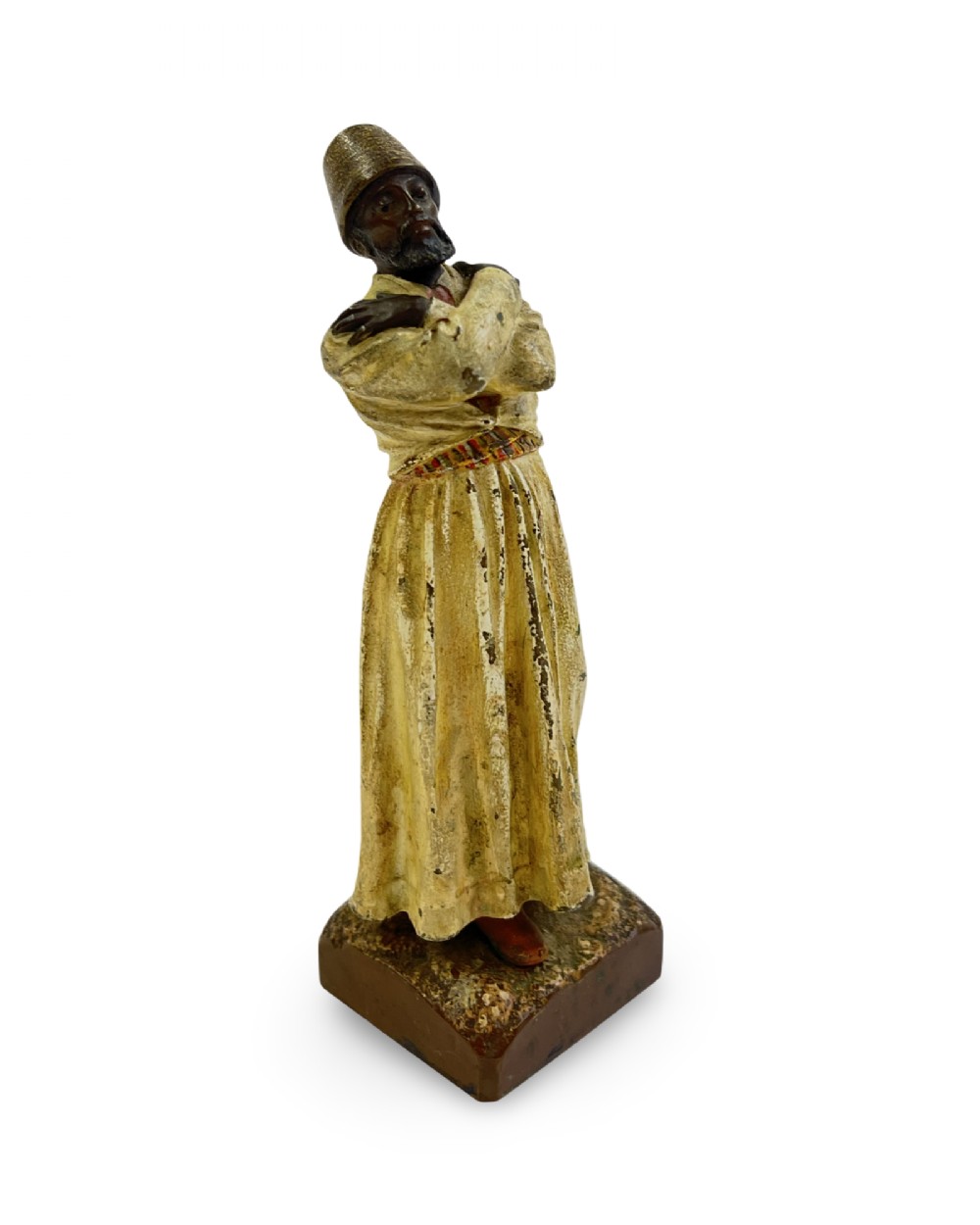 A cold painted bronze statuette depicting a standing whirling dervish with arms crossed, wearing a tall hat and long cream robe. View II