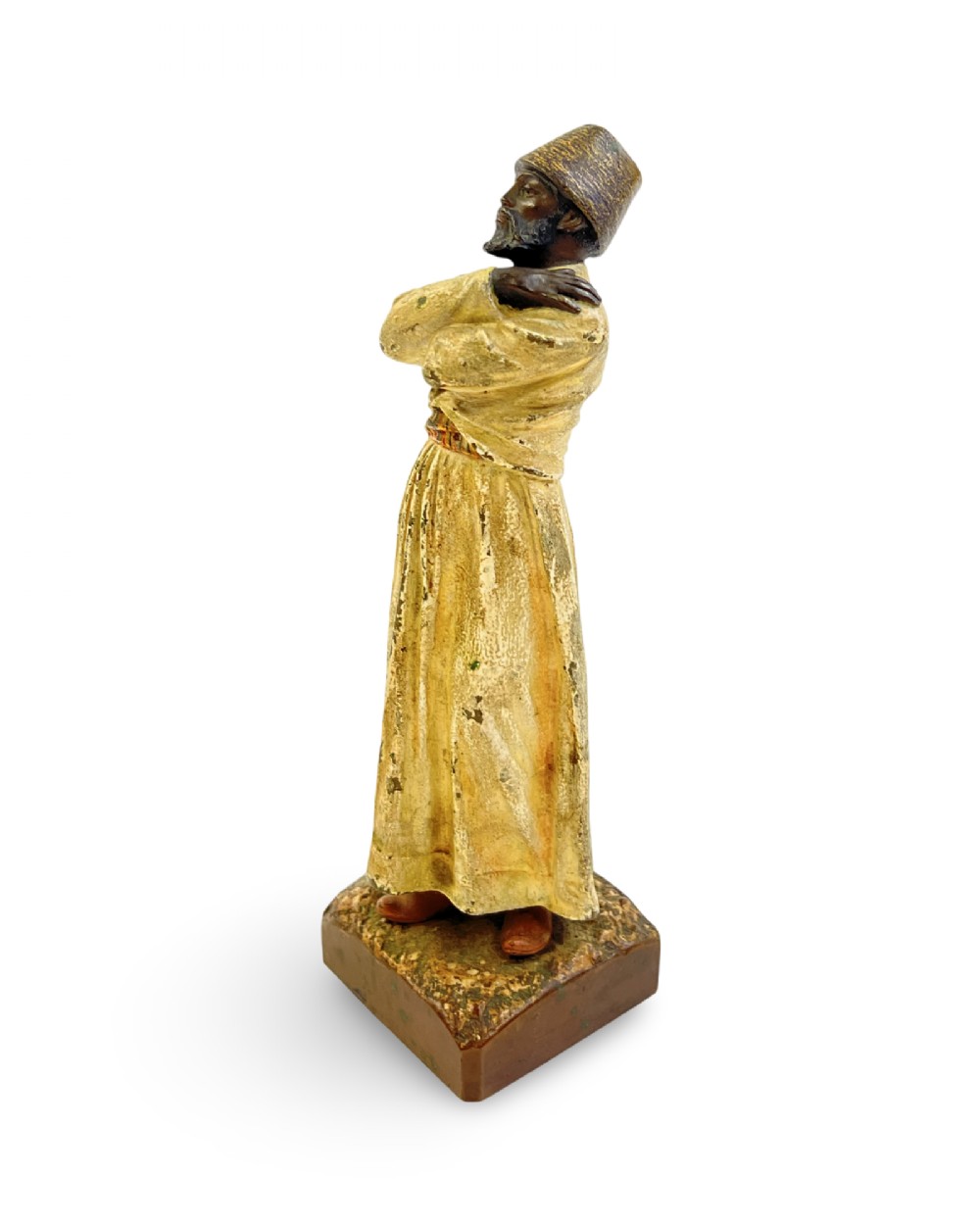 A cold painted bronze statuette depicting a standing whirling dervish with arms crossed, wearing a tall hat and long cream robe. View III