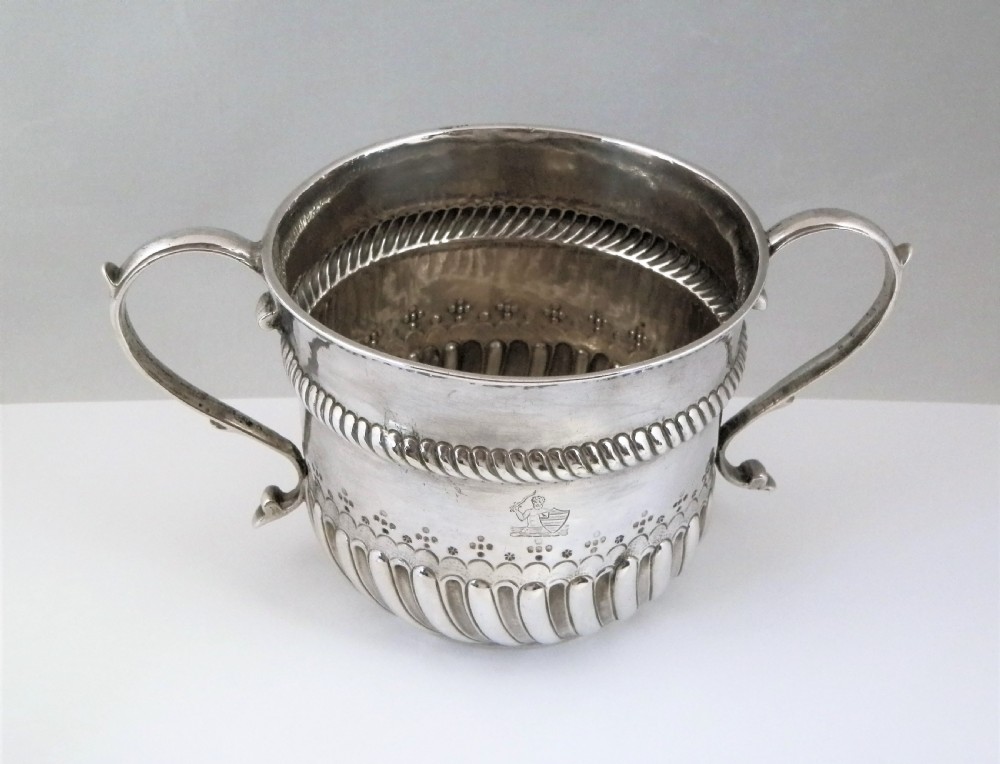 A 1694 William and Mary sterling silver porringer with twin scroll handles, rope-moulded girdle, lower spiral fluting, and an engraved armorial crest. View II