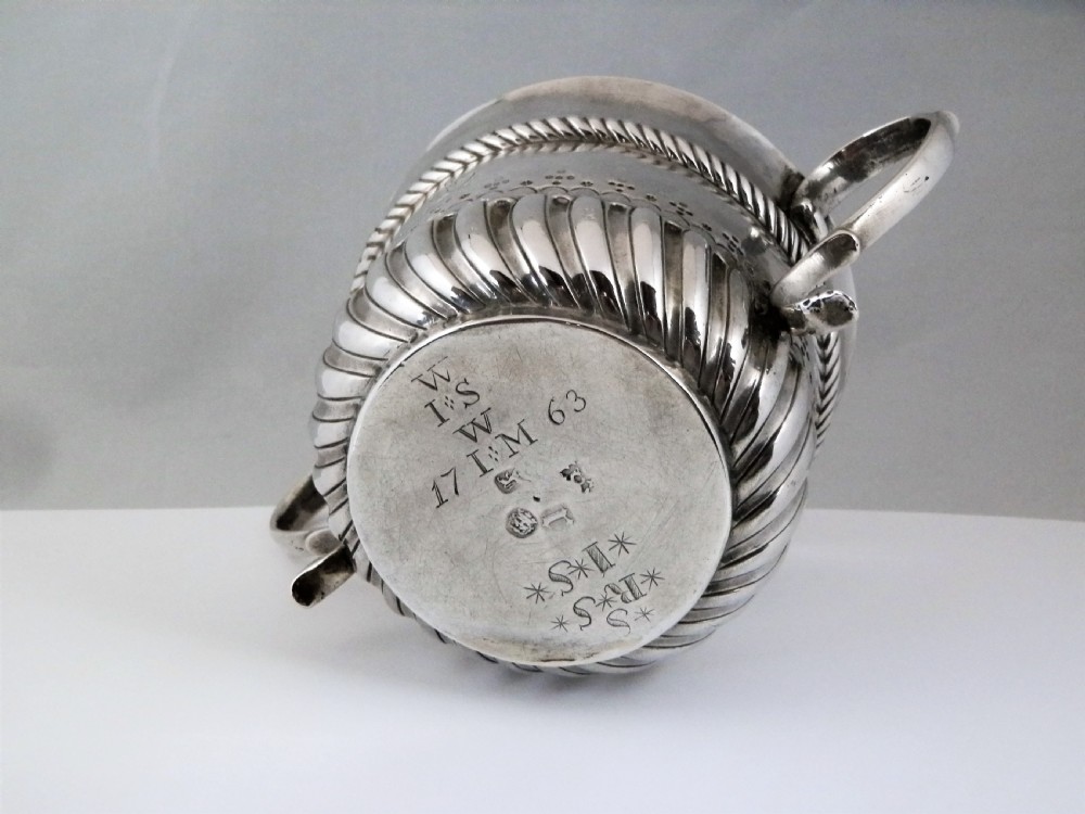 A 1694 William and Mary sterling silver porringer with twin scroll handles, rope-moulded girdle, lower spiral fluting, and an engraved armorial crest. View VI