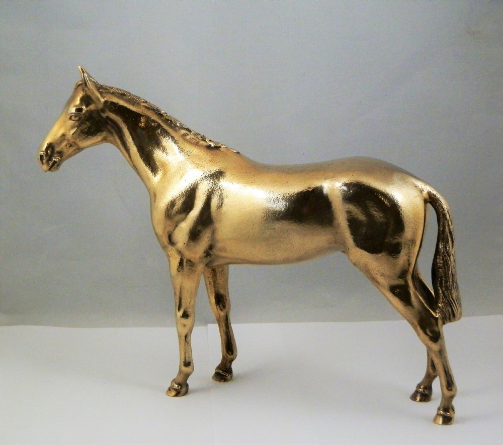 A side-profile view of a gold-coloured silver gilt sculpture depicting a standing racehorse with a detailed mane and muscular structure.