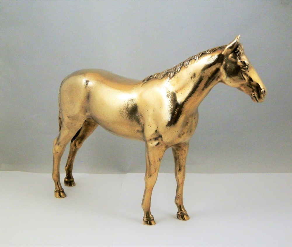 A side-profile view of a gold-coloured silver gilt sculpture depicting a standing racehorse with a detailed mane and muscular structure. View II