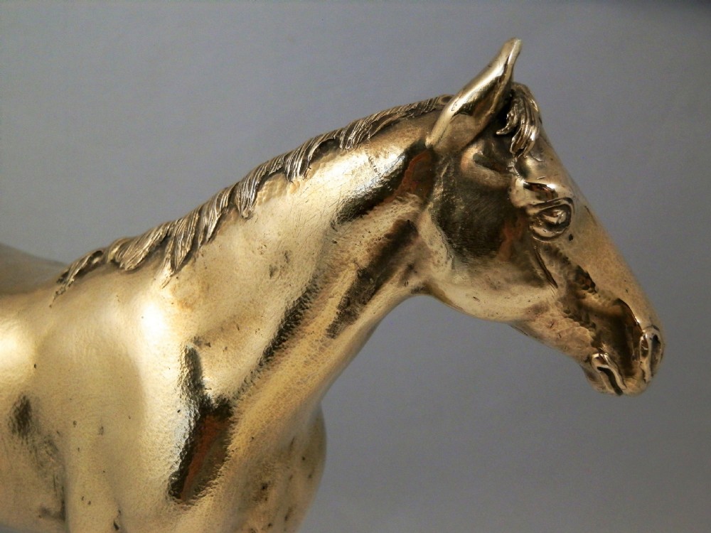 A side-profile view of a gold-coloured silver gilt sculpture depicting a standing racehorse with a detailed mane and muscular structure. View III