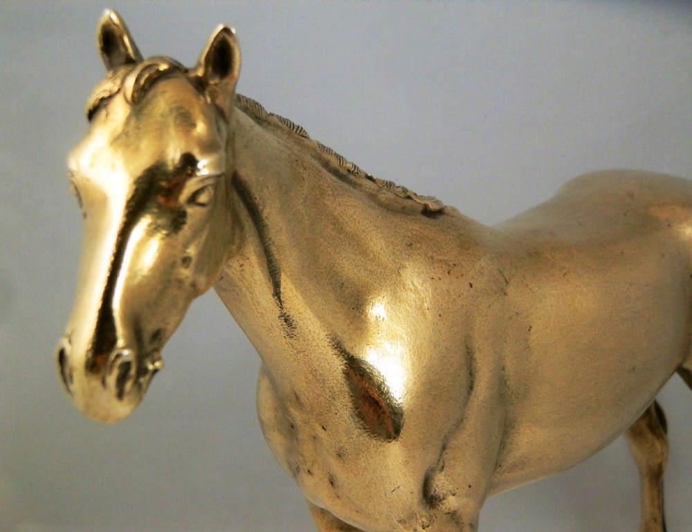 A side-profile view of a gold-coloured silver gilt sculpture depicting a standing racehorse with a detailed mane and muscular structure. View V
