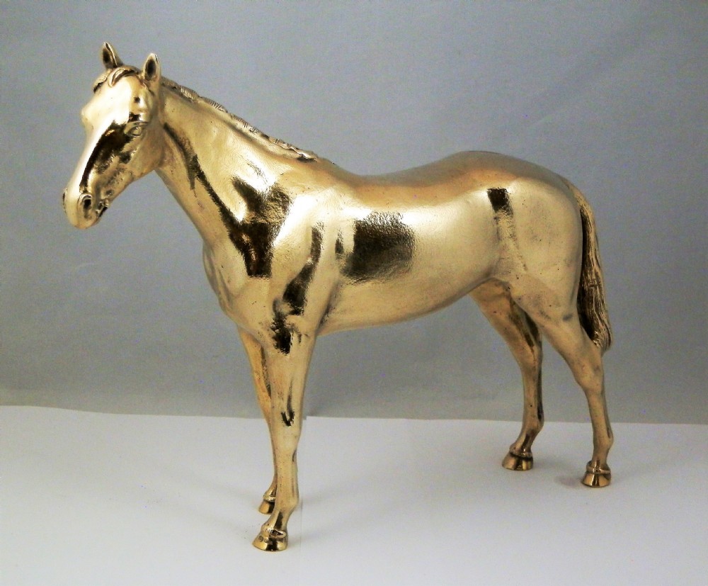 A side-profile view of a gold-coloured silver gilt sculpture depicting a standing racehorse with a detailed mane and muscular structure. View VI