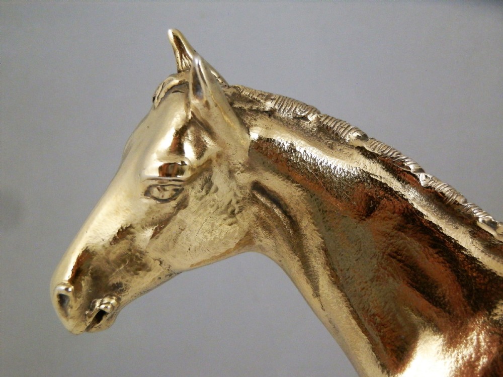 A side-profile view of a gold-coloured silver gilt sculpture depicting a standing racehorse with a detailed mane and muscular structure. View X