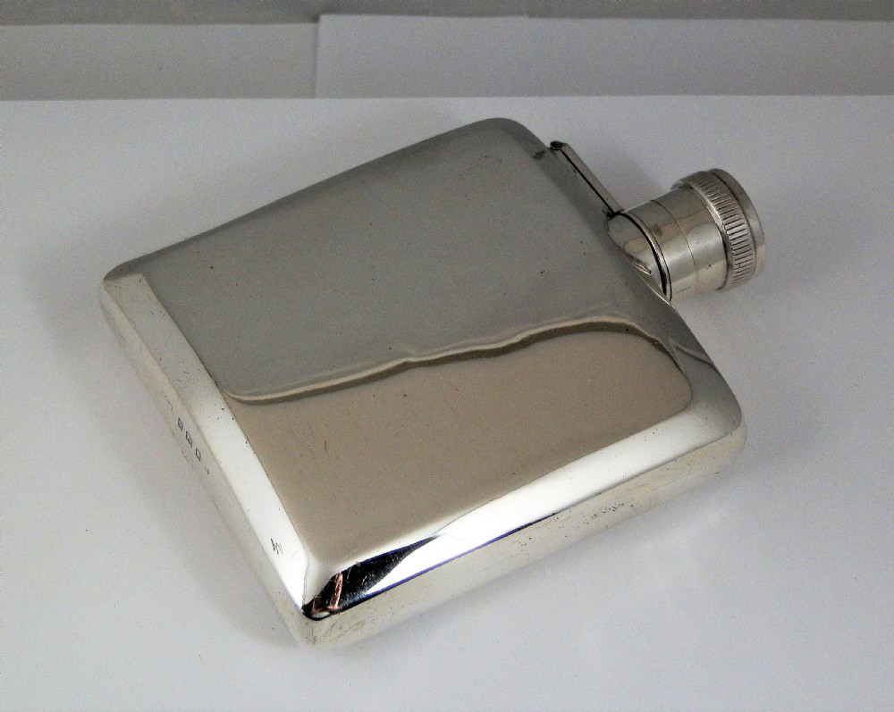A polished rectangular silver Art Deco hip flask featuring a knurled bayonet cap and curved pocket profile. View VI