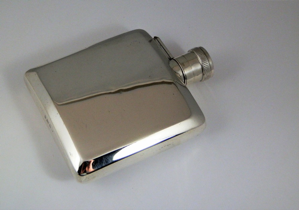 A polished rectangular silver Art Deco hip flask featuring a knurled bayonet cap and curved pocket profile. View VII