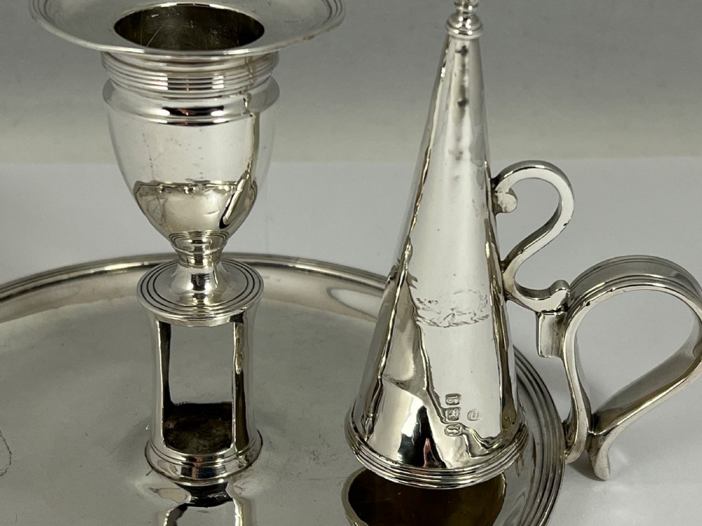 A George III sterling silver chamberstick featuring a circular base pan, a raised central candle socket, a curved side handle, and a removable conical snuffer. View III