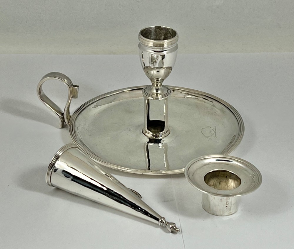 A George III sterling silver chamberstick featuring a circular base pan, a raised central candle socket, a curved side handle, and a removable conical snuffer. View VI