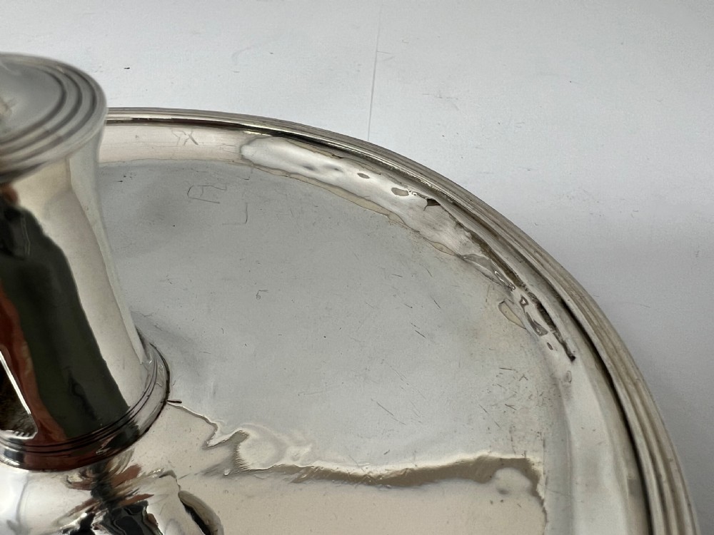 A George III sterling silver chamberstick featuring a circular base pan, a raised central candle socket, a curved side handle, and a removable conical snuffer. View VII